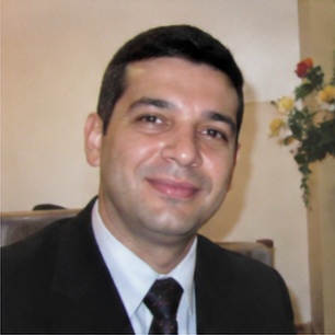 depoimento_1 Um homem de aparência austera, com cabelo longo e barba, se destaca em primeiro plano, expressando-se com intensidade enquanto aponta para a audiência à sua frente. Atrás dele, uma multidão de ouvintes, todos vestidos de forma simples e rústica, observa atentamente suas palavras. O cenário árido, repleto de colinas desérticas, reforça a atmosfera de um chamado urgente à reflexão e mudança. Esse cenário evoca a figura bíblica de João Batista, que prega no deserto e convoca as pessoas a se prepararem para um novo caminho.