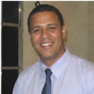 depoimento_6 Um homem de aparência austera, com cabelo longo e barba, se destaca em primeiro plano, expressando-se com intensidade enquanto aponta para a audiência à sua frente. Atrás dele, uma multidão de ouvintes, todos vestidos de forma simples e rústica, observa atentamente suas palavras. O cenário árido, repleto de colinas desérticas, reforça a atmosfera de um chamado urgente à reflexão e mudança. Esse cenário evoca a figura bíblica de João Batista, que prega no deserto e convoca as pessoas a se prepararem para um novo caminho.